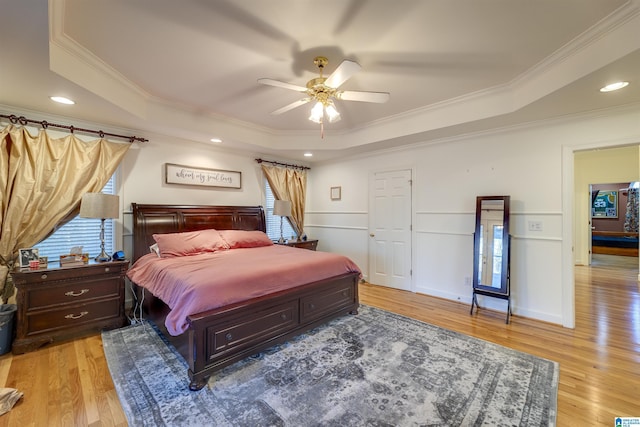 bedroom with crown molding, a raised ceiling, ceiling fan, and light wood-type flooring