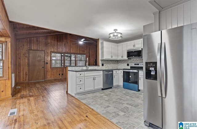 kitchen featuring stainless steel appliances, sink, white cabinets, and wooden walls