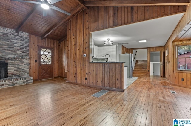 interior space featuring sink, a fireplace, lofted ceiling with beams, light hardwood / wood-style floors, and wood walls