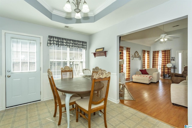 dining space with a tray ceiling, ceiling fan with notable chandelier, ornamental molding, and light hardwood / wood-style floors