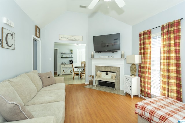 living room featuring a tiled fireplace, ceiling fan, high vaulted ceiling, and light wood-type flooring