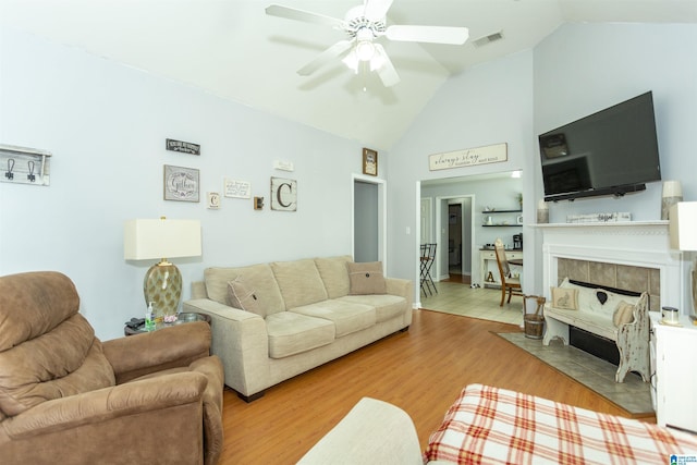 living room featuring ceiling fan, a tiled fireplace, high vaulted ceiling, and light hardwood / wood-style flooring