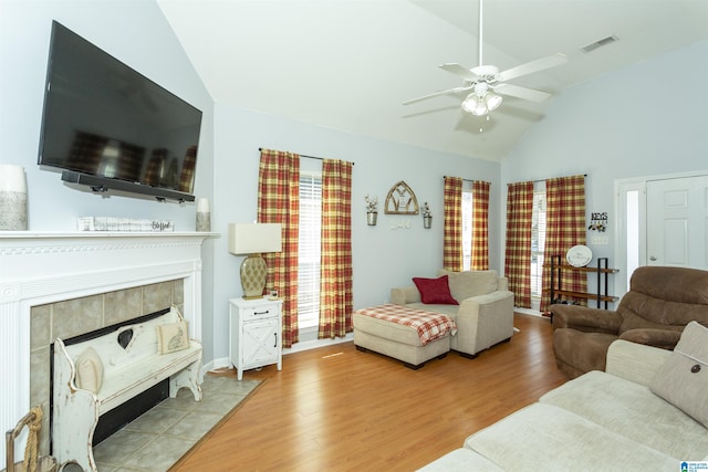 living room featuring ceiling fan, a fireplace, vaulted ceiling, and light wood-type flooring