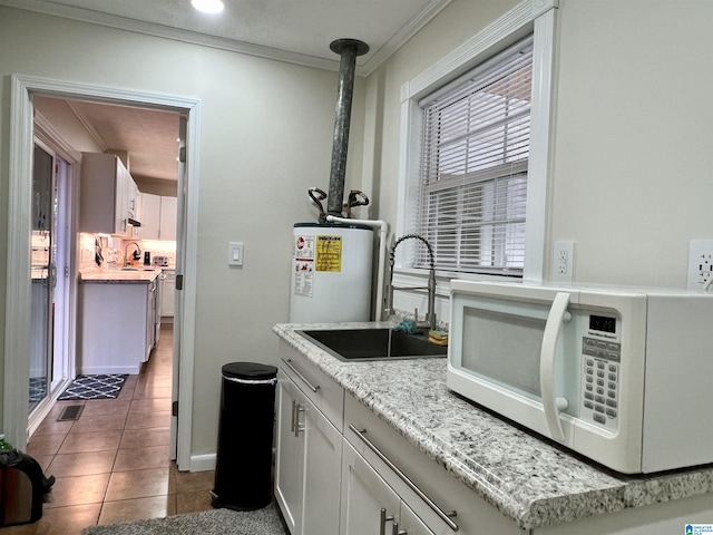 kitchen with sink, light stone counters, ornamental molding, dark tile patterned flooring, and white cabinets