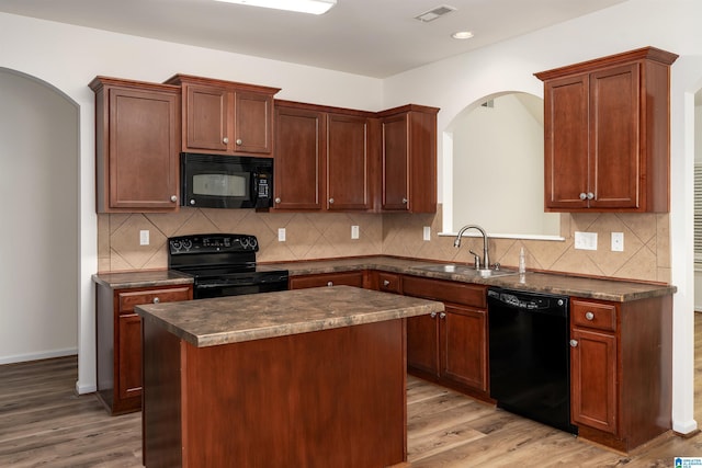 kitchen with sink, black appliances, a center island, hardwood / wood-style floors, and backsplash