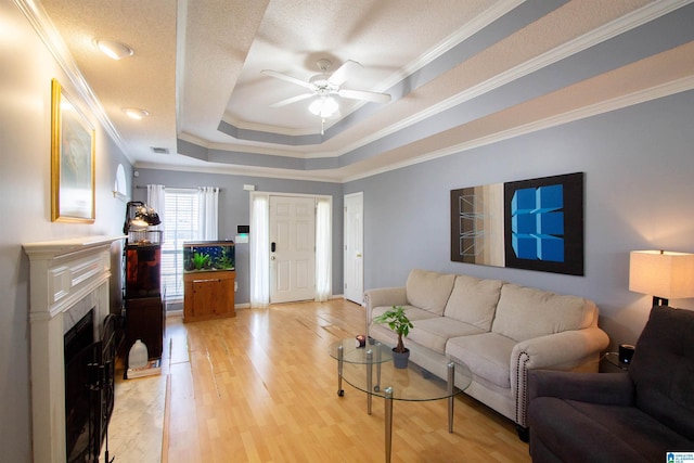 living room with crown molding, light hardwood / wood-style flooring, a tray ceiling, a tile fireplace, and ceiling fan