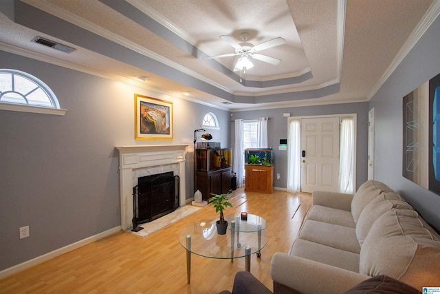 living room with hardwood / wood-style floors, crown molding, ceiling fan, a tray ceiling, and a premium fireplace