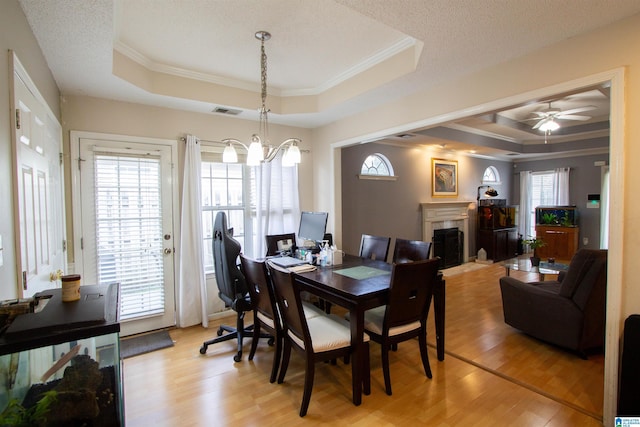 dining area with a raised ceiling, crown molding, and light hardwood / wood-style flooring