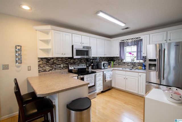 kitchen with appliances with stainless steel finishes, sink, white cabinets, a kitchen bar, and kitchen peninsula