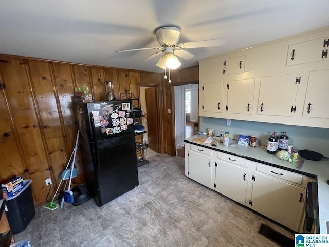 kitchen with white cabinetry, wood walls, ceiling fan, and black fridge