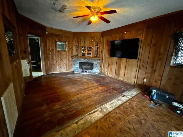 unfurnished living room with wood walls, wood-type flooring, a textured ceiling, ceiling fan, and a fireplace