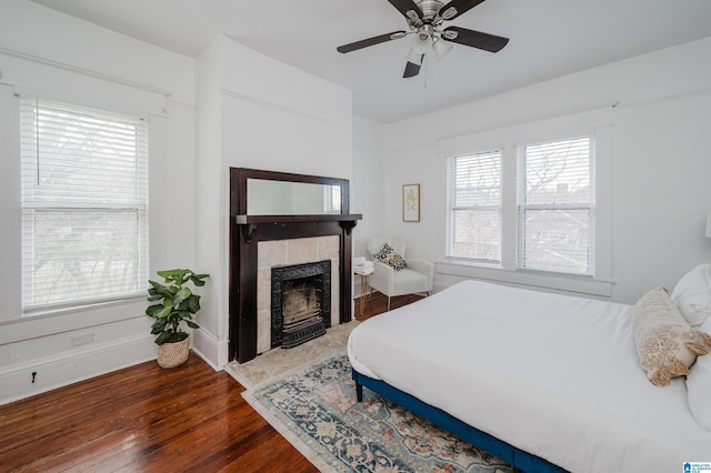 bedroom featuring a fireplace, dark wood-type flooring, and ceiling fan