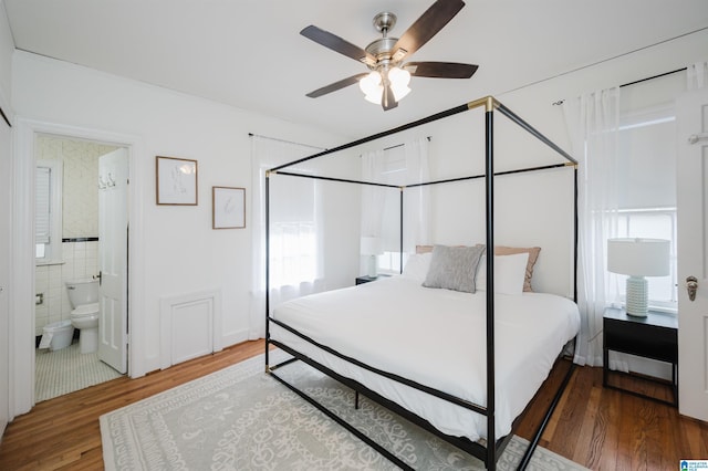 bedroom featuring hardwood / wood-style flooring, ensuite bath, ceiling fan, and tile walls