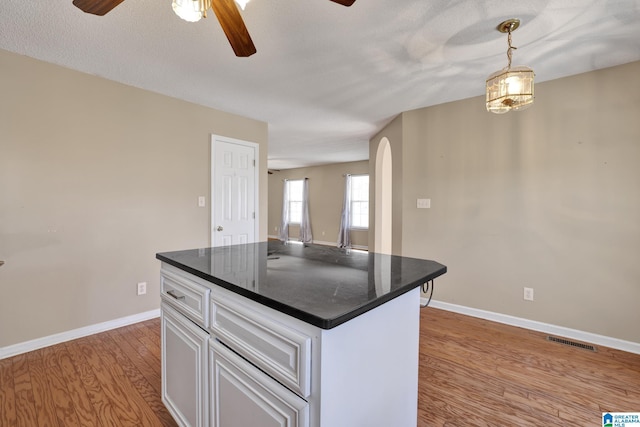 kitchen featuring white cabinetry, a center island, hanging light fixtures, light wood-type flooring, and ceiling fan