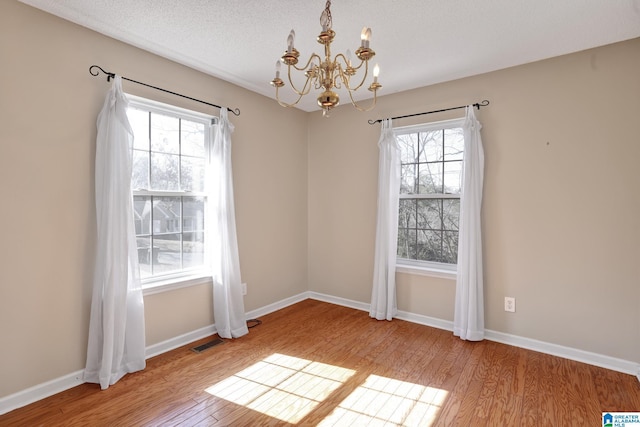 unfurnished dining area with a notable chandelier, a textured ceiling, and light wood-type flooring