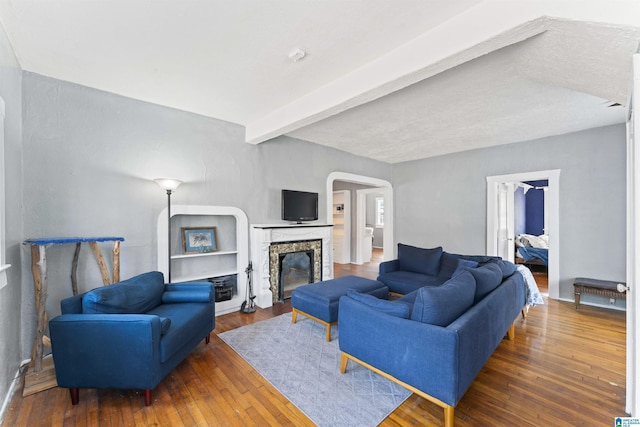 living room featuring a stone fireplace, dark wood-type flooring, and beam ceiling