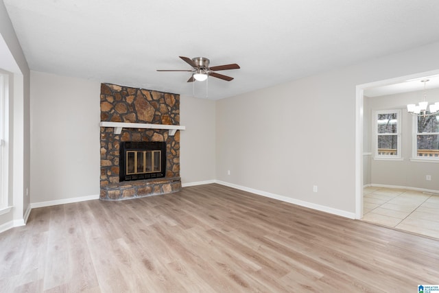 unfurnished living room featuring light hardwood / wood-style flooring, ceiling fan with notable chandelier, and a fireplace