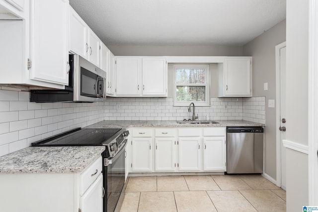 kitchen with white cabinetry, appliances with stainless steel finishes, sink, and light stone counters