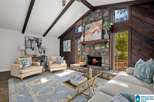 living room with beam ceiling, high vaulted ceiling, wood-type flooring, a stone fireplace, and wood walls