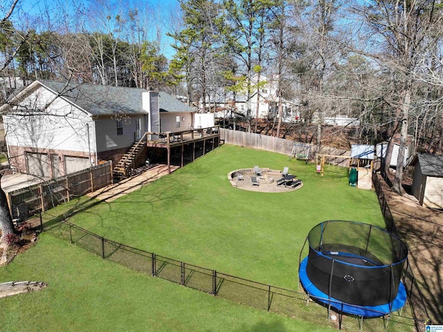 view of yard featuring a trampoline, a wooden deck, and an outdoor fire pit