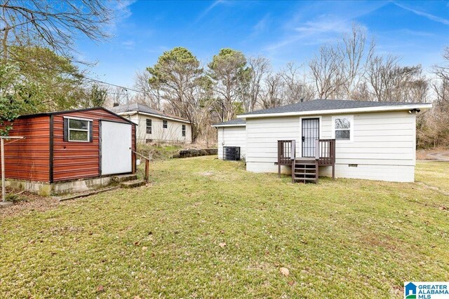 back of house featuring a storage unit, central AC unit, and a lawn