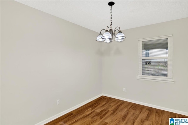 empty room featuring hardwood / wood-style flooring, a chandelier, and a textured ceiling