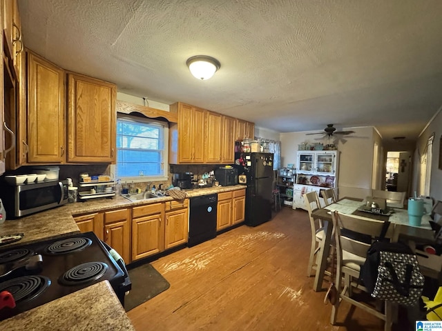 kitchen featuring light wood-type flooring, black appliances, brown cabinetry, and a sink