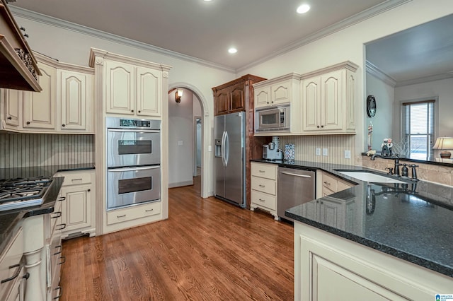 kitchen with sink, kitchen peninsula, stainless steel appliances, dark wood-type flooring, and cream cabinetry