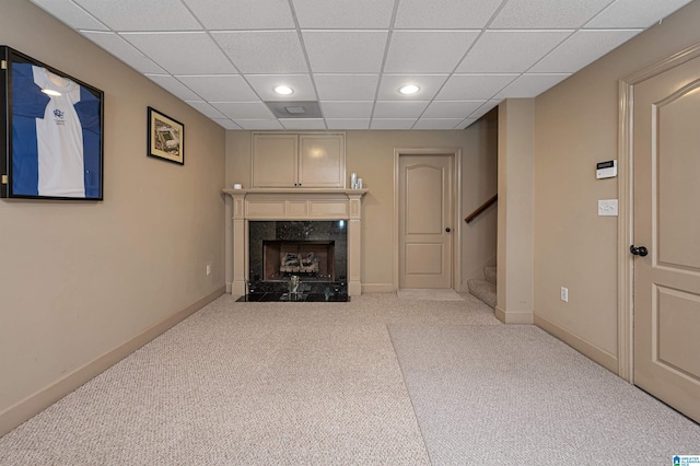 living room with a drop ceiling, a high end fireplace, and light colored carpet