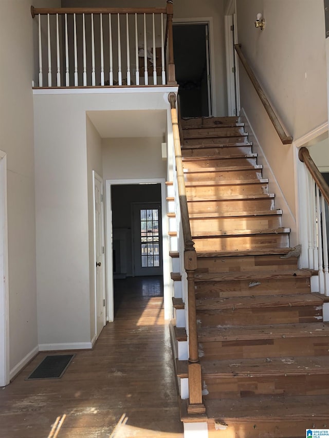 stairway with wood-type flooring and a high ceiling