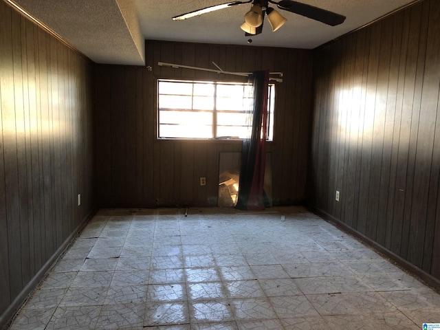 spare room featuring ceiling fan, wooden walls, and a textured ceiling