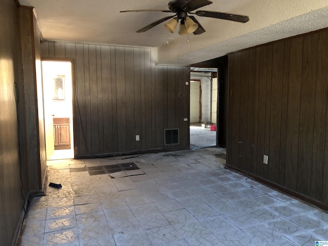 spare room with ceiling fan, a textured ceiling, and wooden walls