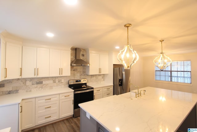 kitchen with appliances with stainless steel finishes, decorative light fixtures, white cabinetry, light stone countertops, and wall chimney exhaust hood