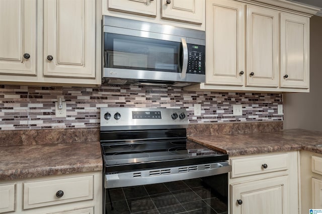 kitchen with dark countertops, cream cabinetry, appliances with stainless steel finishes, and tasteful backsplash