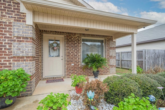 view of exterior entry with brick siding and fence