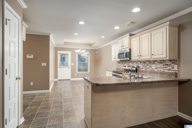 kitchen featuring dark countertops, backsplash, cream cabinets, stainless steel appliances, and a raised ceiling