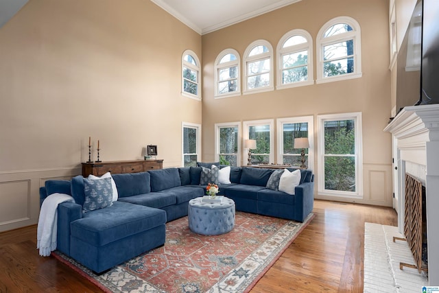 living room featuring crown molding, a towering ceiling, wood-type flooring, and a brick fireplace