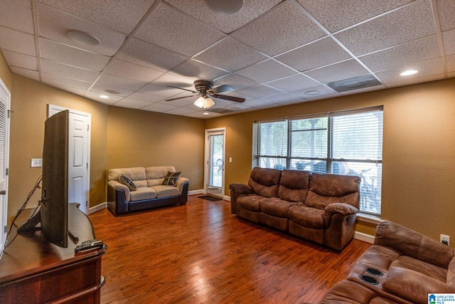 living room featuring dark wood-type flooring, ceiling fan, and a drop ceiling