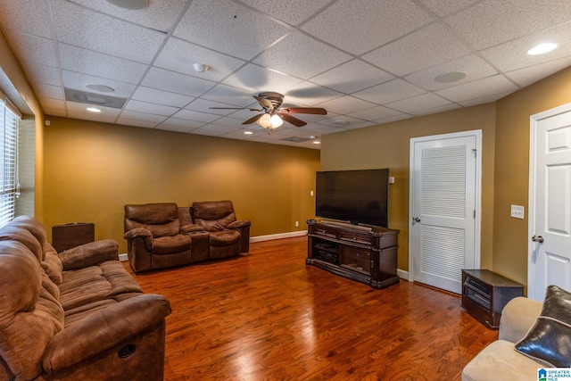 living room with dark hardwood / wood-style flooring, a drop ceiling, and ceiling fan