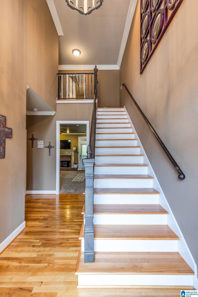 staircase with a brick fireplace, crown molding, and wood-type flooring