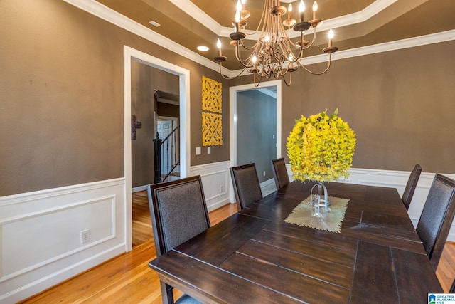 dining area with hardwood / wood-style floors, crown molding, a chandelier, and a raised ceiling