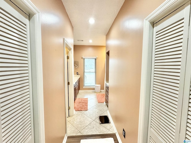 hallway with a textured ceiling and light tile patterned floors