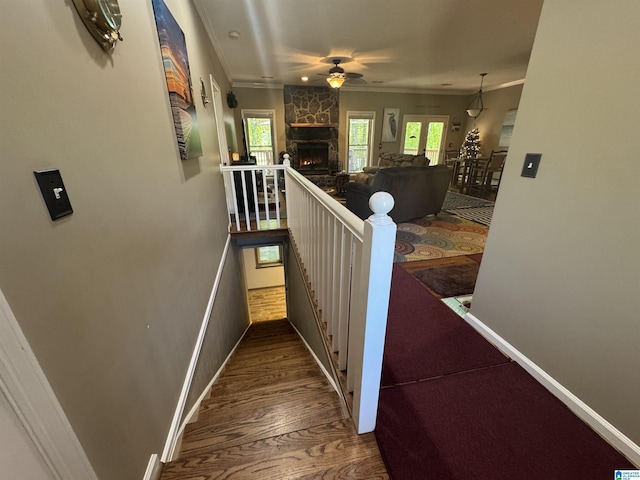 stairway with crown molding, a ceiling fan, a stone fireplace, wood finished floors, and baseboards