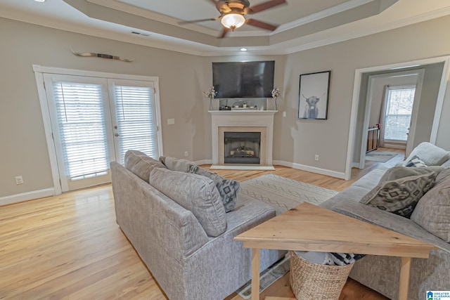 living room featuring crown molding, ceiling fan, a tray ceiling, and light hardwood / wood-style flooring