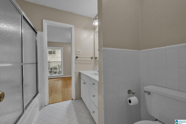 full bathroom featuring combined bath / shower with glass door, tile walls, vanity, tile patterned floors, and toilet