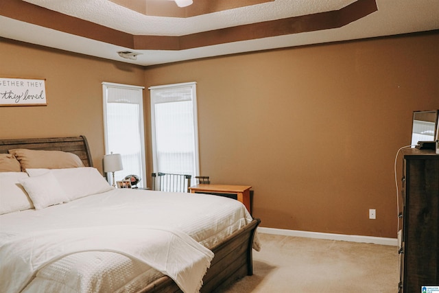 bedroom with light colored carpet and a tray ceiling