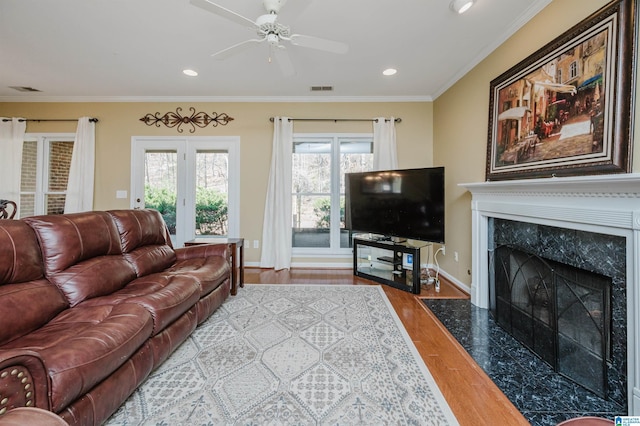 living room with light hardwood / wood-style floors, ornamental molding, a premium fireplace, and ceiling fan