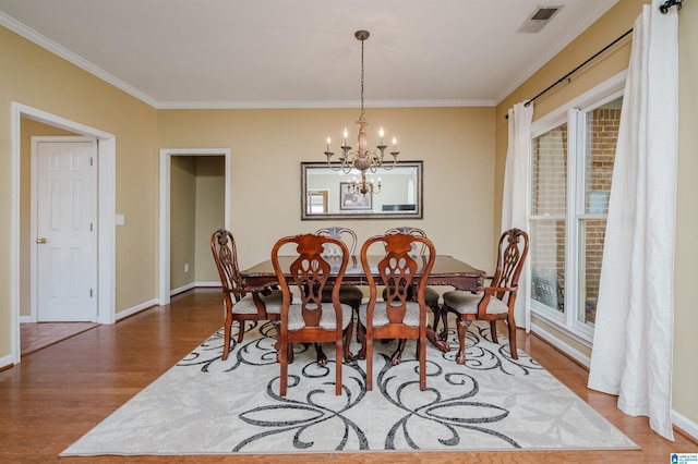 dining area with hardwood / wood-style flooring, a healthy amount of sunlight, ornamental molding, and an inviting chandelier