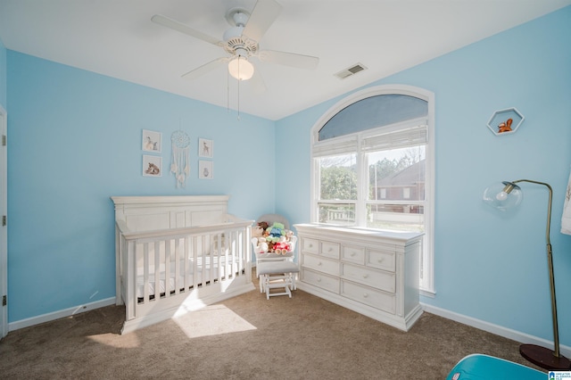 bedroom featuring a crib, dark colored carpet, and ceiling fan