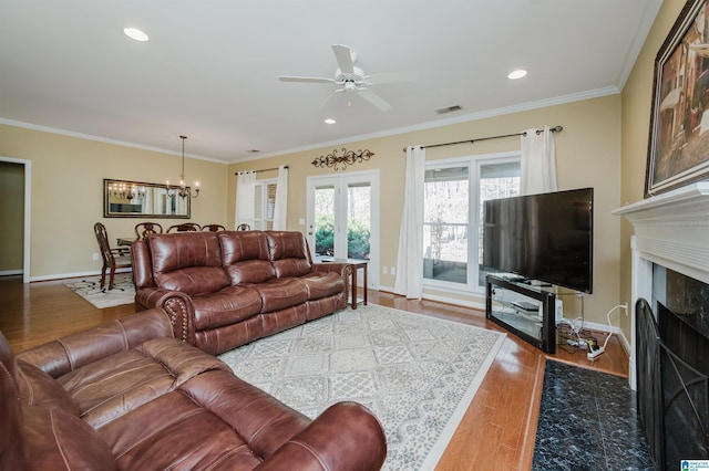 living room with hardwood / wood-style flooring, ornamental molding, a premium fireplace, and ceiling fan with notable chandelier